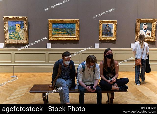 People sitting in the Metropolitan Museum Of Art with Paul Cezanne paintings behind