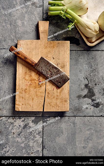 A meat cleaver on a chopping board next to fennel bulbs