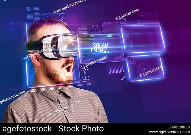 Businessman looking through Virtual Reality glasses with SOLAR ENERGY inscription, new technology concept