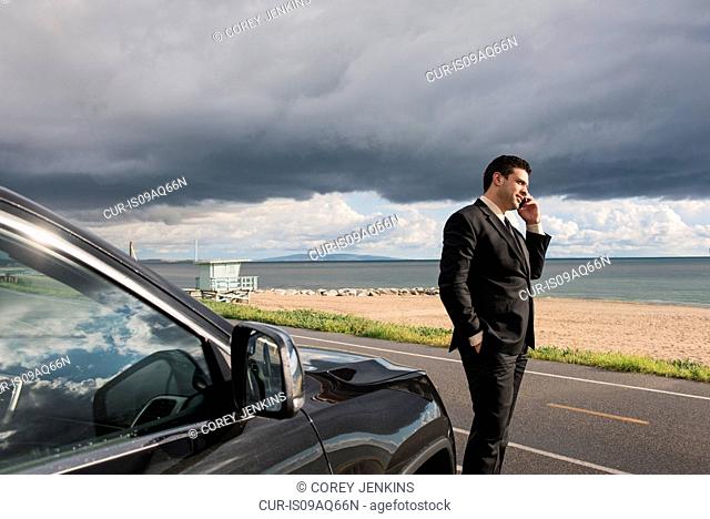 Businessman talking on smartphone at coastal parking lot