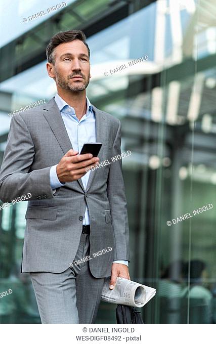 Portrait of businessman with cell phone and newspaper on the go