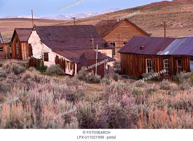 Old wooden houses at dawn, with Sierra Nevada snow-tipped mountain range in distance, sage brush foreground, Bodie pioneer village, California