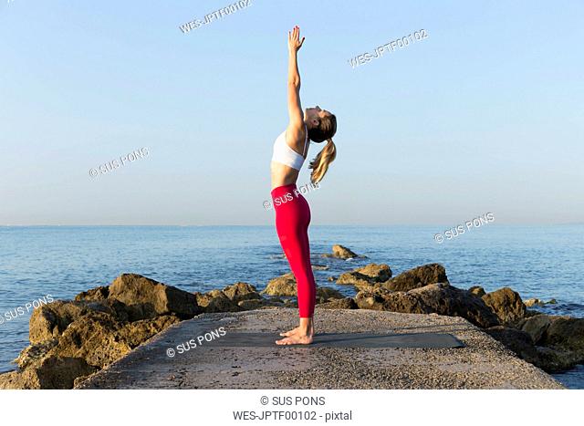 Young woman practicing yoga on the beach, doing sun salutations
