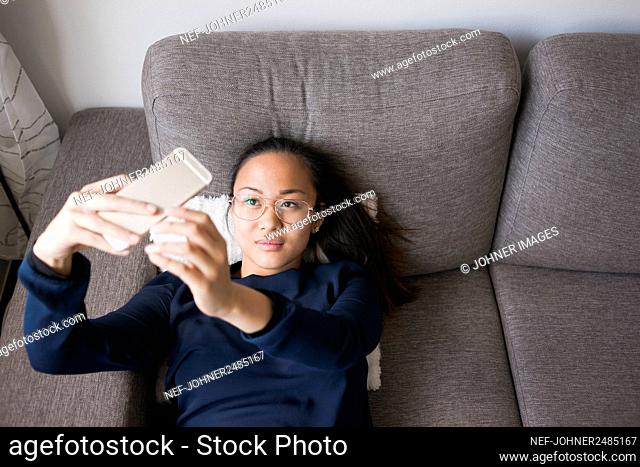 Woman lying on sofa and taking selfie