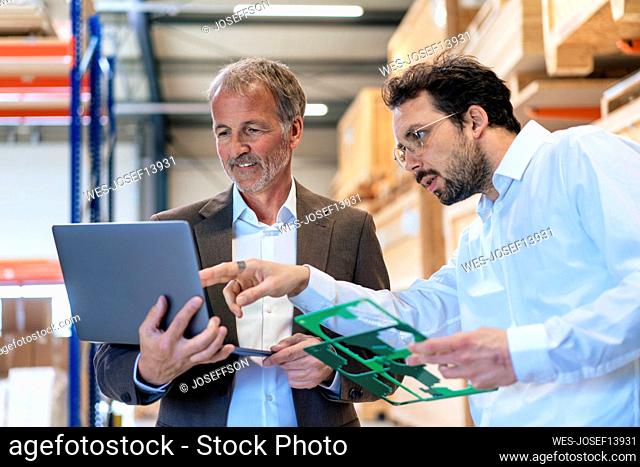 Senior businessman with colleague discussing over laptop at warehouse