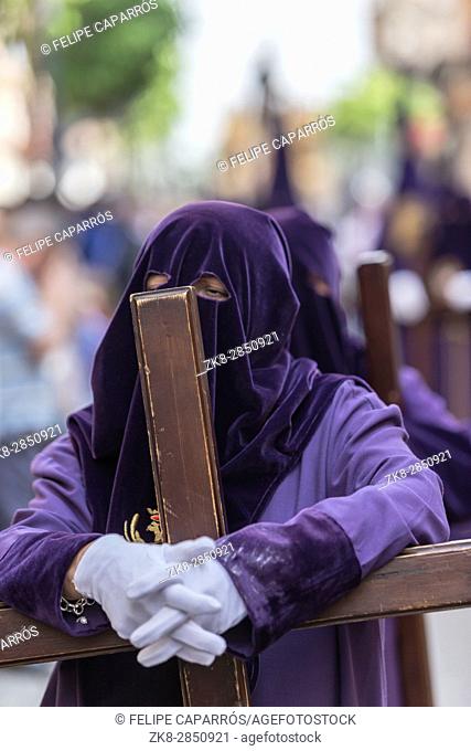 Penitent dressed in purple tunic of velvet resting on wooden cross during atonement station on Holy Week, Andalusia, Spain