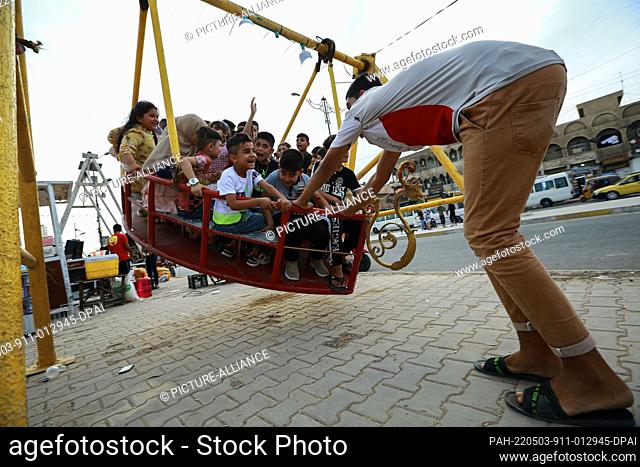 03 May 2022, Iraq, Baghdad: A man pushes a big swing with several children at an amusement park in Sadr City district as they celebrate on the second day of the...