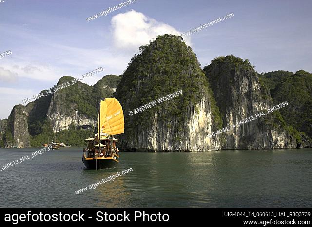 Traditional style cruising junk under sail approaches rocky islands of Halong Bay Vietnam