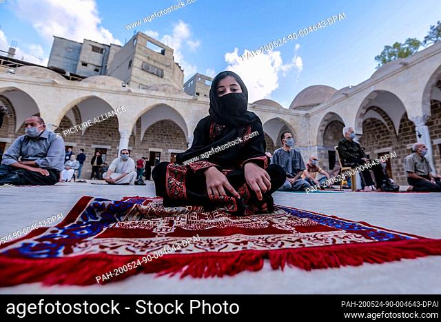 24 May 2020, Palestinian Territories, Gaza City: A little girl wearing a scarf and a face mask takes part in Eid al-Fitr prayer in a mosque marking the end of...