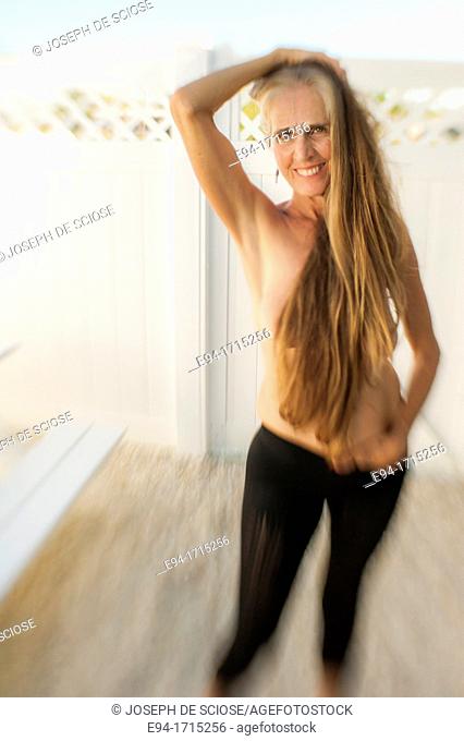 Partially nude 57 year old woman with long hair smiling at the camera