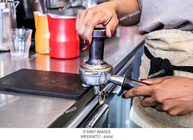 Woman barista preparing coffee beans grounds, tamping them down into a grounds holder in a cafe