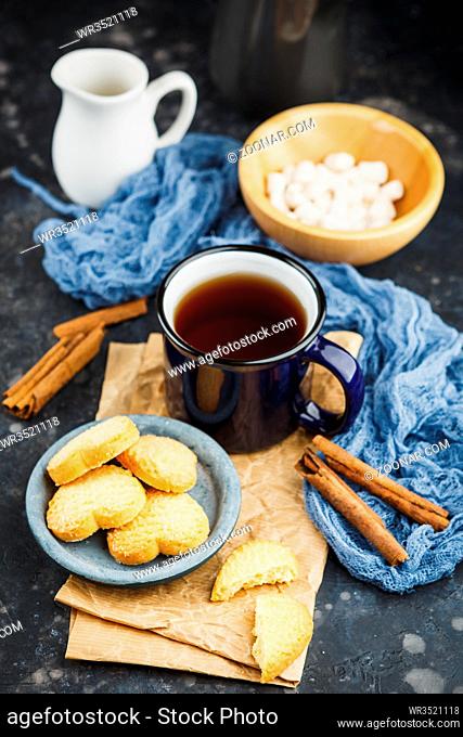 Blue enamelled cup of tea, cinnamon sticks, anise stars and shortbread on a dark background