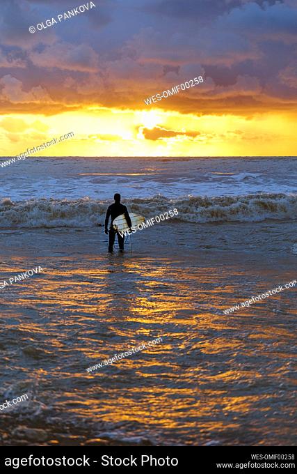 Man with surfboard looking at dramatic sky over sea