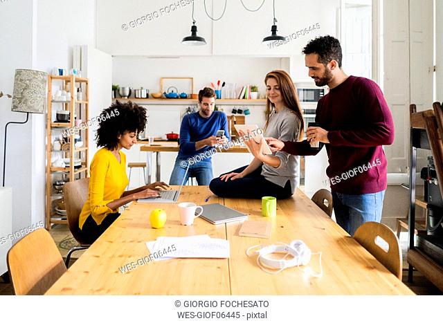 Four friends in dining room at home with portable devices