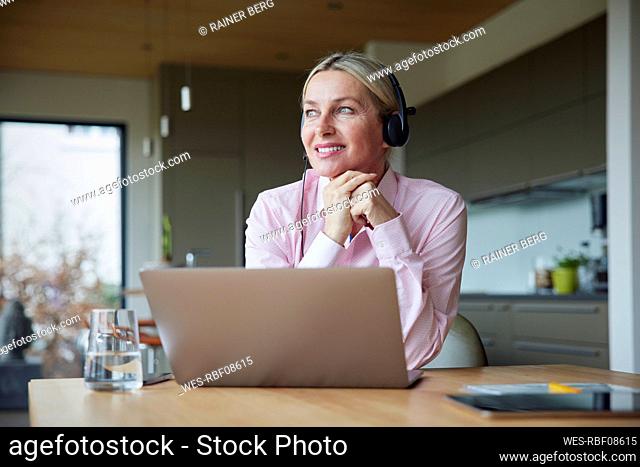 Smiling woman wearing headphones sitting with hand on chin at table