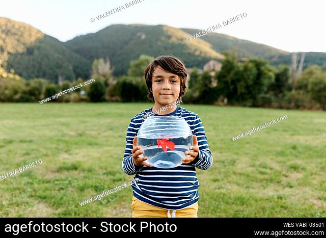 Smiling boy holding fishbowl in hand while standing at back yard