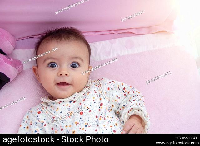 Interrogative and surprised expression of a young baby in the cradle
