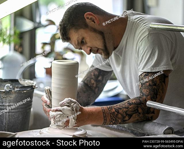 25 July 2023, Berlin: Manufacturer Timm Langhoff uses his hands to turn the porcelain mass that is being formed into a vase at the Königliche...