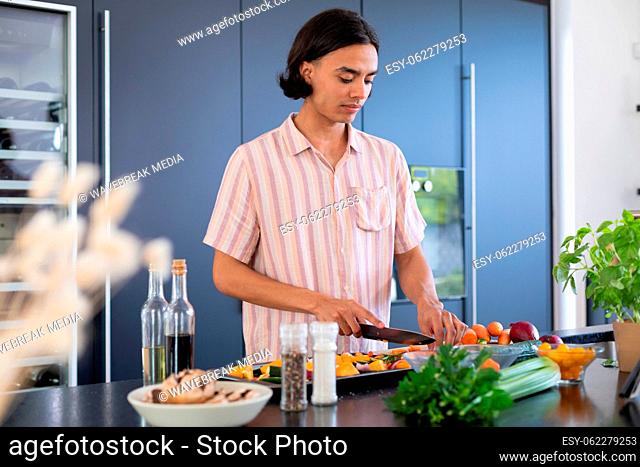 Happy biracial man cooking, chopping vegetables in kitchen