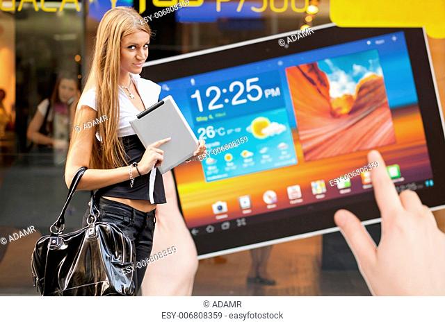 Young Woman with tablet computer walking on street, downtown. In background is blured advertisiment with OpenSource graphics. Visible noise
