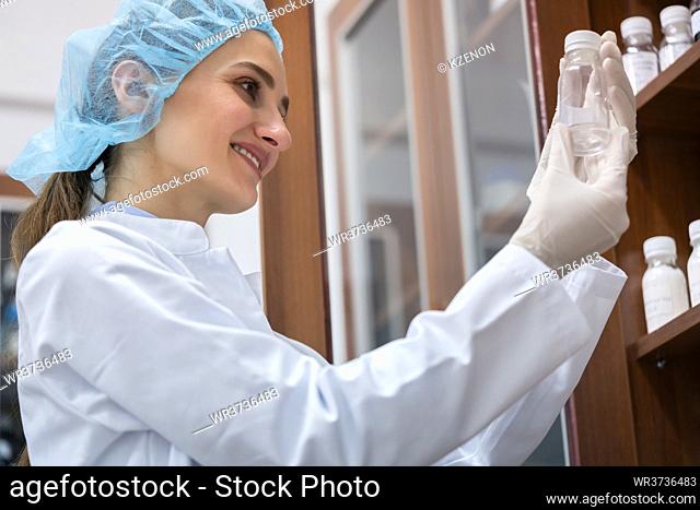 Low-angle side view of a female chemist happy for finding the perfect chemical substance during experimental work in the laboratory of a cosmetics factory