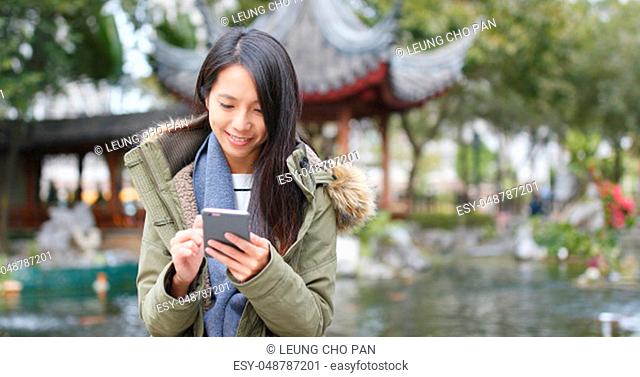 Young woman using mobile phone, sending sms and reply group chat on app at china, Chinese pavilion garden
