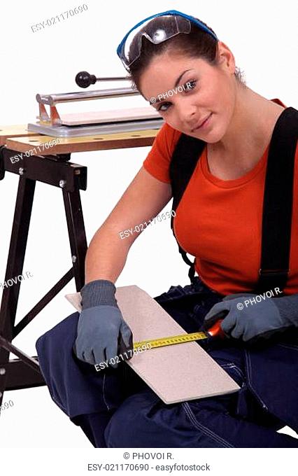 A woman measuring a tile before cutting it