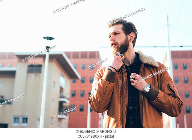 Young male hipster stroking beard on housing estate