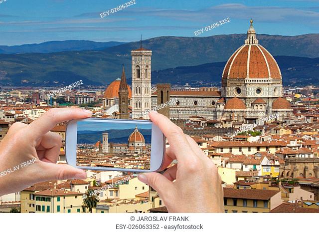 In the bottom left of the photo are hands holding smart phone and taking picture of a historical center and cathedral in Florence (Tuscany, Italy)
