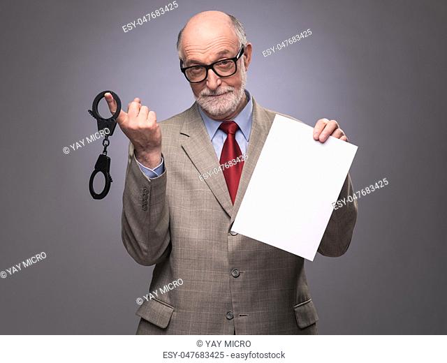 Senior business man with handcuffs and blank contract paper hints at danger of financial crimes