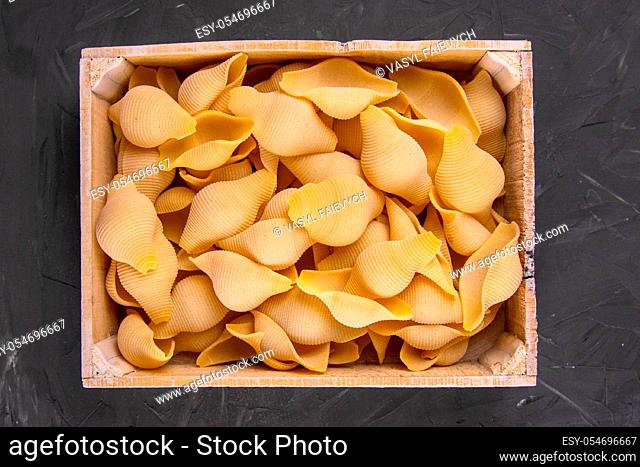 Raw pasta shells in wooden box on a black wooden background . Top views close-up