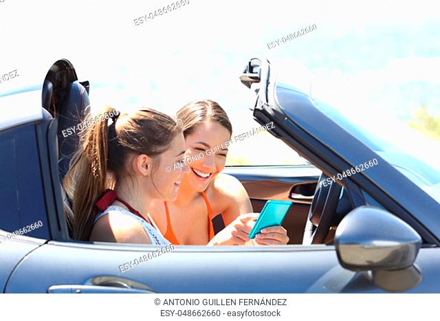 Two happy friends reading phone content inside a convertible car on summer vacation