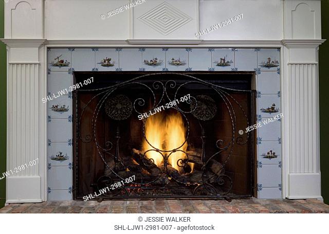 FIREPLACES: Straight on view antique tile surround on classical styled fireplace mantel.scroll work fireplace screen, brick hearth, fluted columns, gas fire