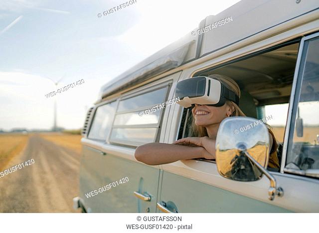 Smiling woman wearing VR glasses leaning out of window of a camper van