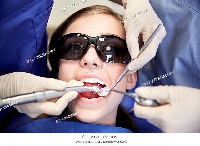 people, medicine, stomatology and health care concept - female dentists with mirror, drill and probe treating patient girl teeth at dental clinic office