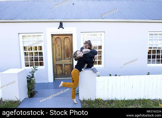 Brother and sister outside their home, tickling each other