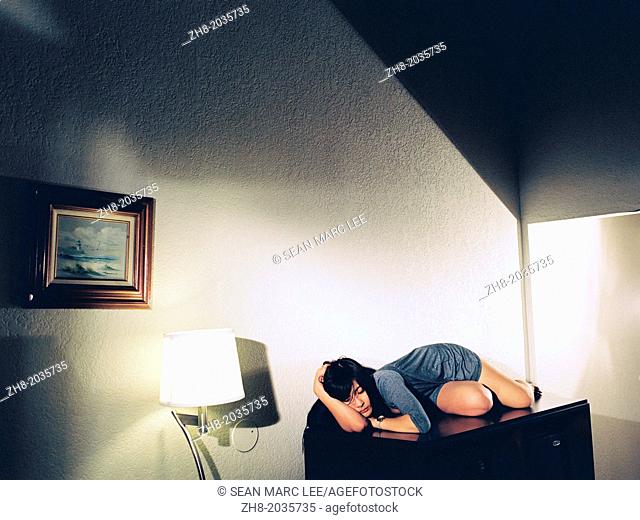 A young woman lies seductively and mysteriously on a cabinet in a room
