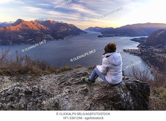 A girl staring at the view of the center and the two branches of Lake Como during a windy winter sunset from Breglia. Plesio, Como Lake, Lombardy, Italy
