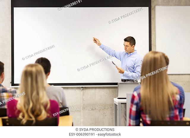 education, high school, technology and people concept - teacher with notepad, laptop computer standing in front of students and showing something on white board...
