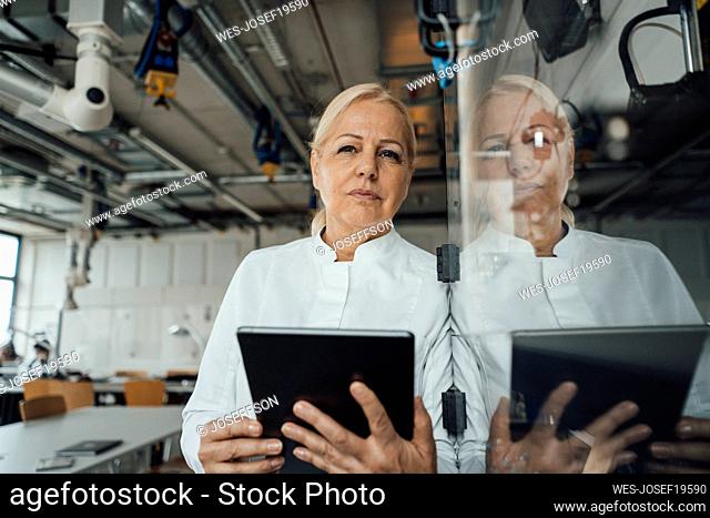 Thoughtful scientist with tablet PC standing by glass cabinet