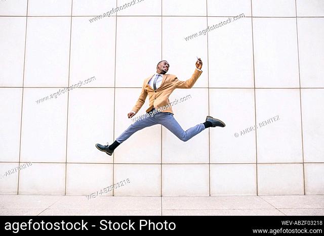 Young businessman jumping and taking a selfie in front of a wall