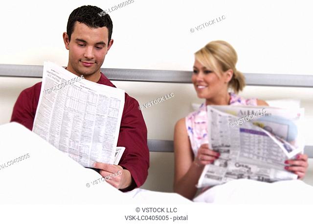 Couple in bed reading newspaper