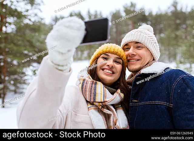 couple with smartphone taking selfie in winter