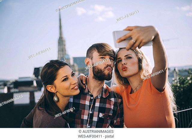 Austria, Vienna, three friends taking selfie on rooftop terrace with Stephansdom in the background