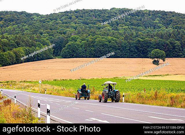 24 July 2021, Lower Saxony, Negenborn: Two men are driving tractors on a country road in the Holzminden district in dreary summer weather