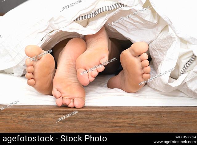 close up feet of a couple under the white sheets blanket in bed, sex hugging and partner valentines concept sexy and romantic