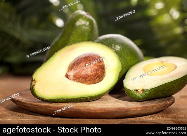 Avocado Essential Oil on tropical green leaves background and wooden table. Horizontal. Front view