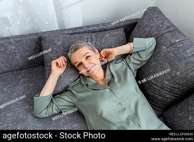 Smiling mature woman lying on couch in living room