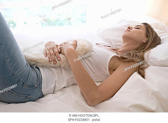 Young woman on bed with hot water bottle on tummy
