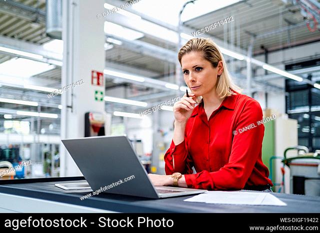 Focused businesswoman with hand on chin looking at laptop in factory